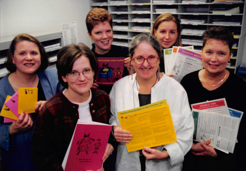 Deborah Wexler and five coworkers holding copies of Vaccine Adults, Vaccinate Women, and Needle Tips newsletters.